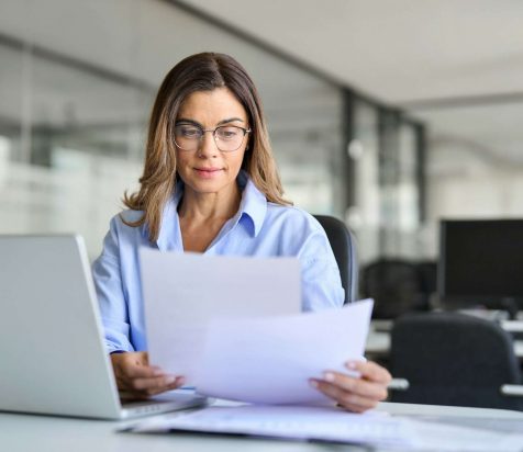 Busy business woman of middle age working on laptop checking documents.