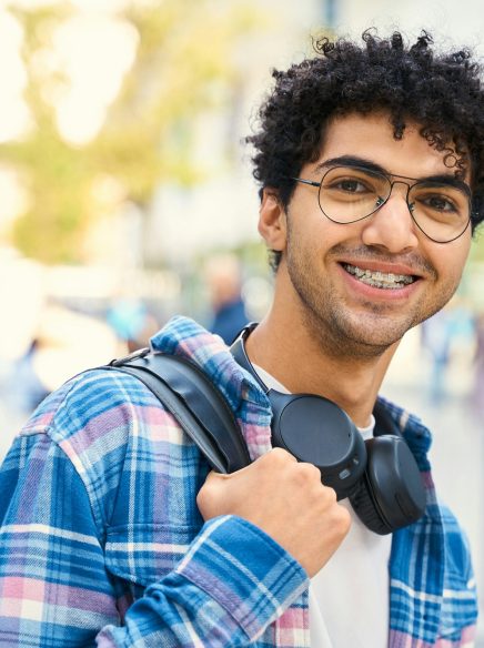 Egyptian student wearing headphones smiling to the camera standing with backpack. Education concept