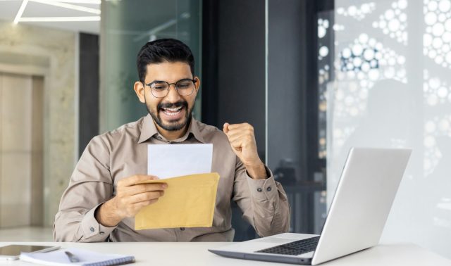 Excited businessman reading good news letter at the office desk