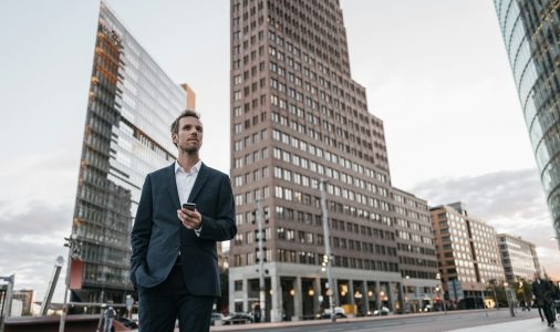 Germany, Berlin, businessman with smartphone standing at Potsdamer Platz