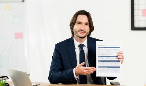 handsome recruiter gesturing while holding resume in office