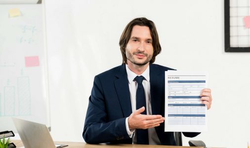 handsome recruiter gesturing while holding resume in office